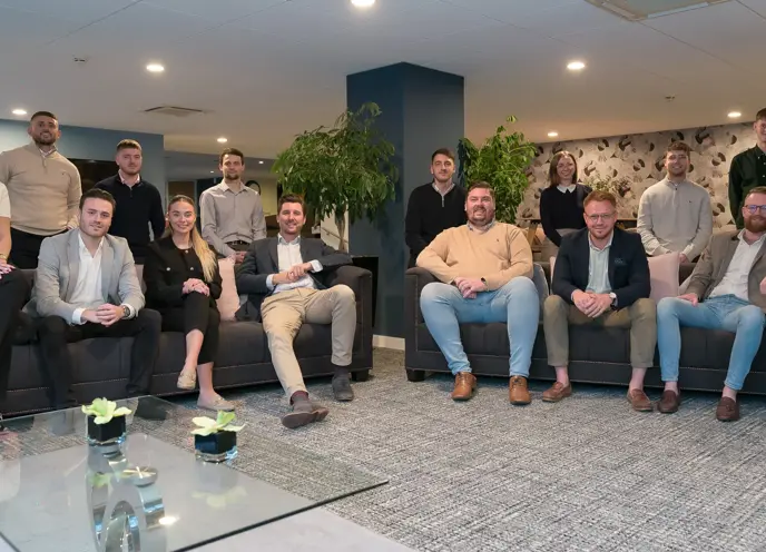 A group of professional individuals sat on sofas in a formal office setting posing for the photo.